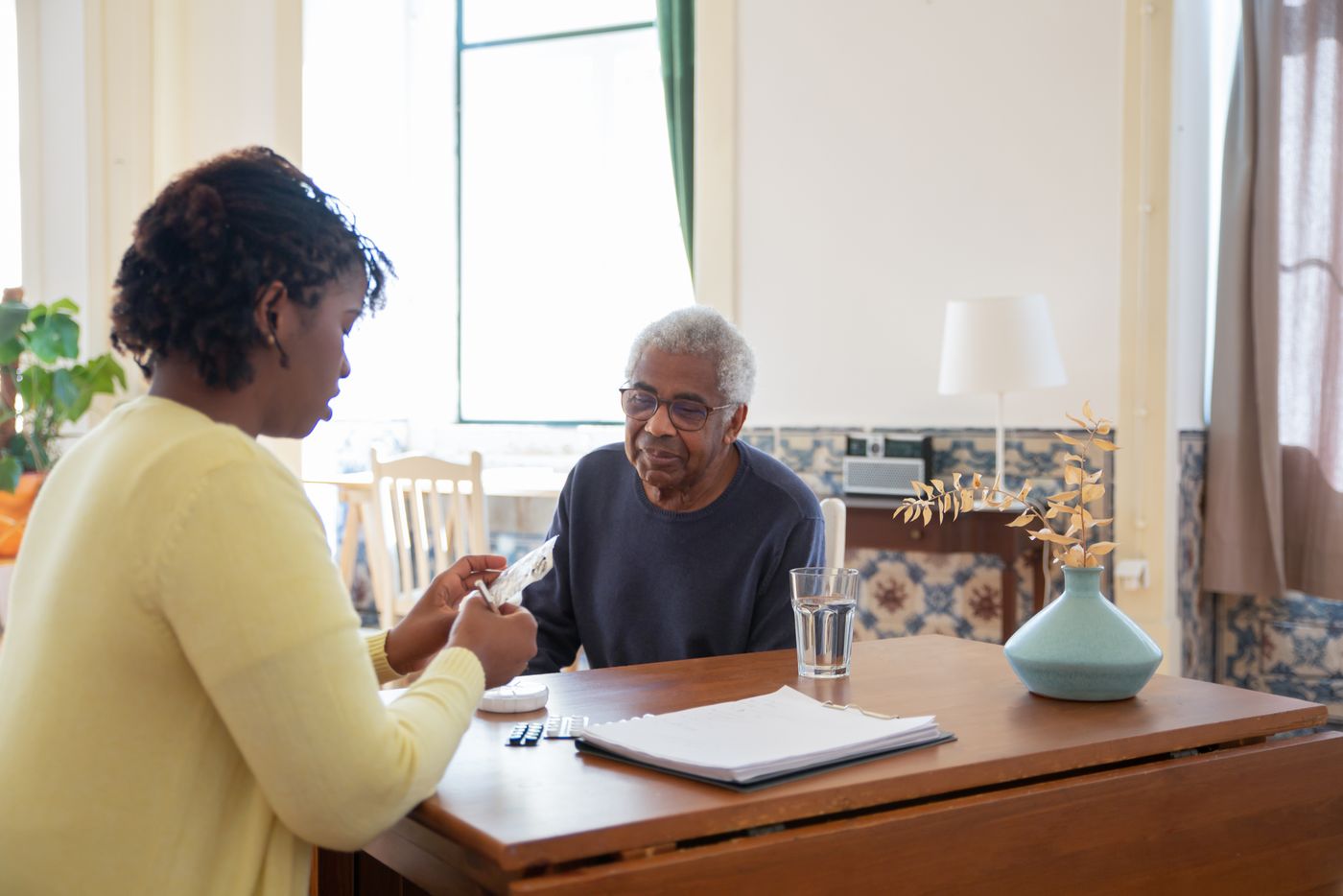 A care professional reviewing medications with an older adult at a kitchen table
