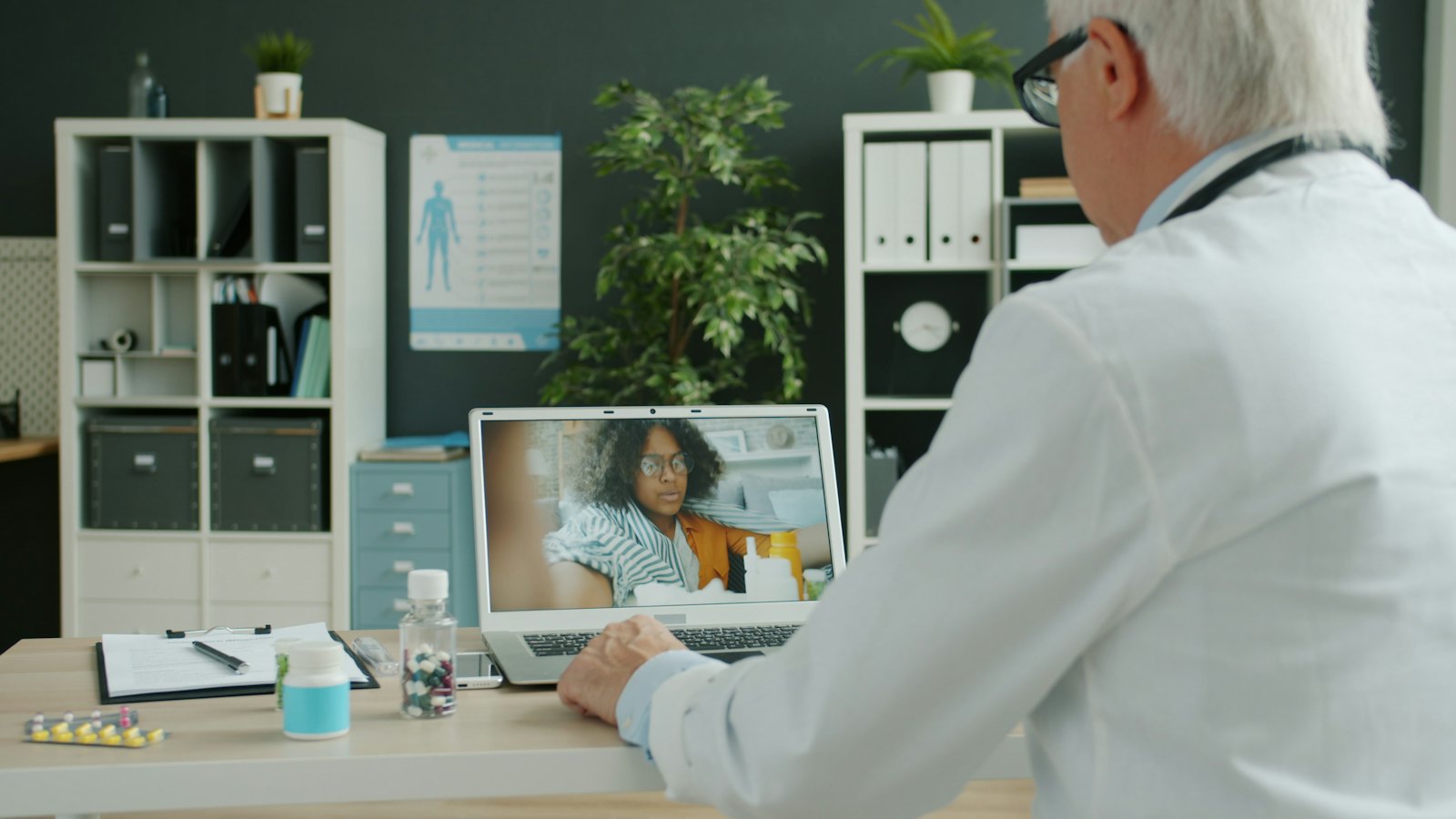A doctor at his desk talks with a patient on a video call.