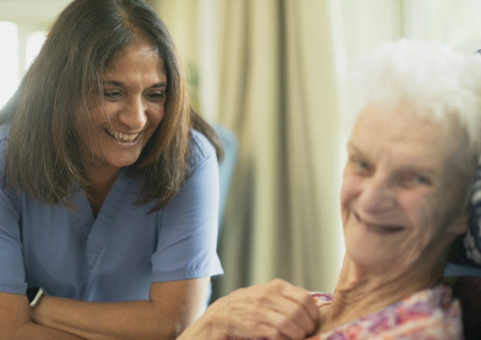 A caregiver and an older woman smile at each other.