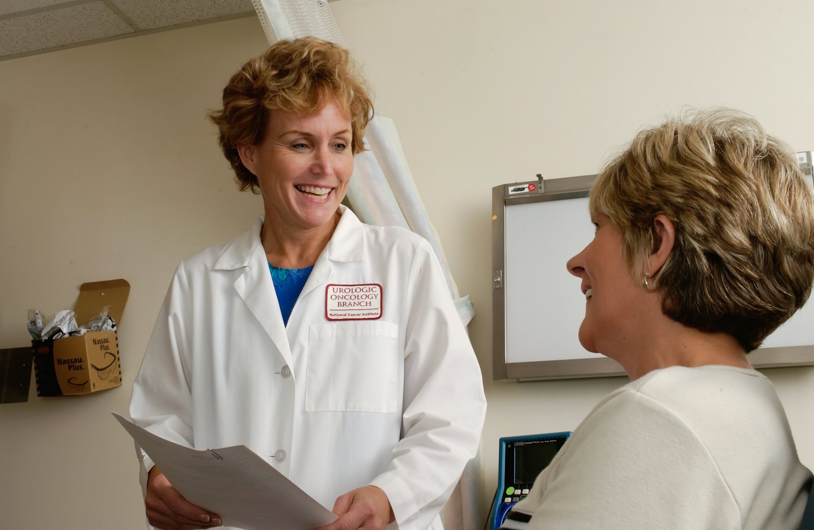 A smiling clinician in a white coat talks with a patient in a clinic.
